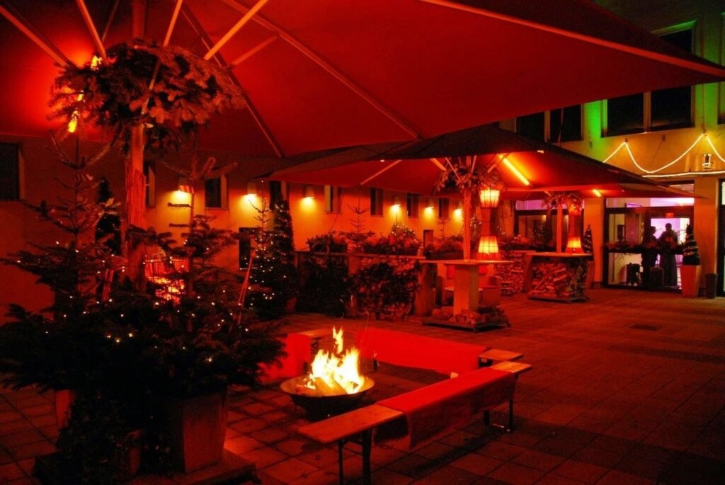 Winterliche Terrasse des Restaurant St. Erhard am Abend mit Feuerschale, Christbäumen, Stehtischen und Schirmen